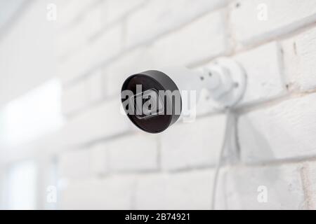 Surveillance ip camera mounted on the white brick wall indoors. Home video surveillance concept Stock Photo