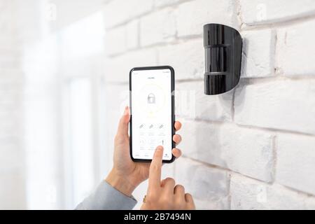 Controlling alarm system with smart phone and special mobile application wireless, holding device the motion sensor indoors Stock Photo