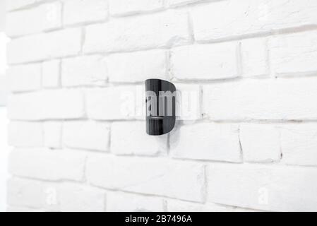 Black wireless motion sensor of alarm system mounted on the white brick wall indoors Stock Photo
