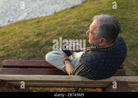 Senior man sitting on a bench in the seaside and holding his phone Stock Photo