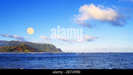 A scenic view of the moonset over the  Pacific Ocean and the Na Pali Mountains along the Na Pali Coast on the island of Kauai, Hawaii. Stock Photo