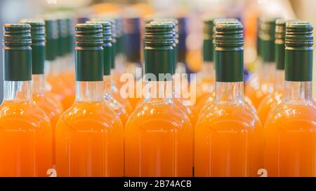 Close up of several glass bottles filled with an orange colored alcoholic drink. E. g. peach, apricot, orange or a similar taste. Probably sweet. Stock Photo