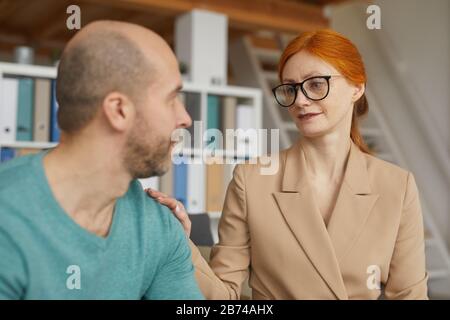 Young red haired psychologist in eyeglasses talking to her patient during therapy at office Stock Photo