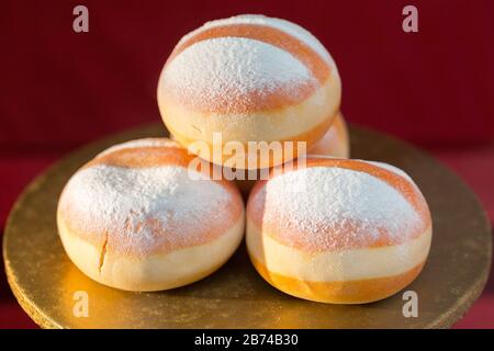View on a pile of three Krapfen (austrian doughnuts). Illuminated by sunlight. With powdered sugar on top. Austrian speciality. Stock Photo