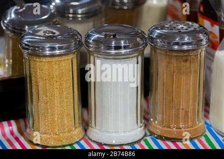 Three glass jars with metallic top filled with white sugar, brown sugar and cinnemon. For sweetening or giving a special taste to hot beverages. Stock Photo