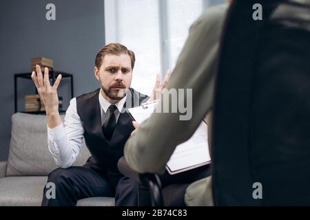 Emotional man talking about feelings at therapist office Stock Photo