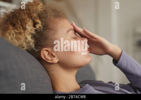 Young woman with curly hair lying on sofa with headache she is very tired Stock Photo