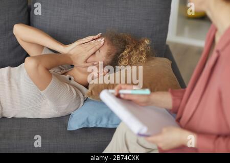 Depressed young woman lying on sofa and telling about her problems to psychologist at the office Stock Photo