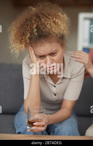 Young depressed woman sitting on sofa and drinking alcohol at home Stock Photo