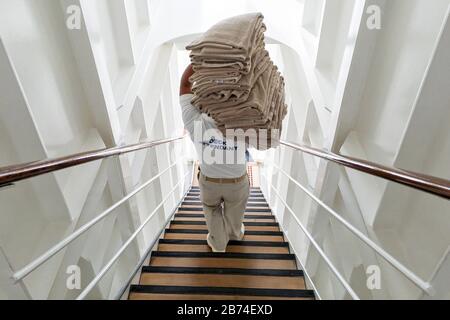 Crossing the Atlantic Ocean from Brooklyn to Southampton onboard the ocean liner Queen Mary 2. A deck hand carries towels for the waiting passengers on the aft main deck. Stock Photo