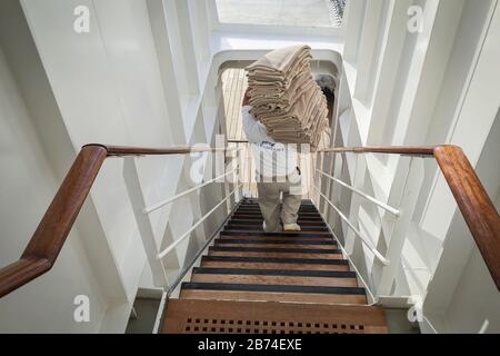 Crossing the Atlantic Ocean from Brooklyn to Southampton onboard the ocean liner Queen Mary 2. A deck hand carries towels for the waiting passengers on the aft main deck. Stock Photo