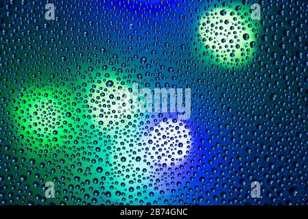 Closeup photo of shiny small circles of water drops on wet dark blue window with city lights Stock Photo