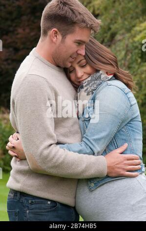 Young pregnant woman cuddling with her partner, outdoors Stock Photo