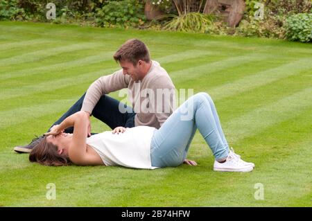 Beautiful pregnant young woman lying down on the grass with her partner sitting next to her Stock Photo