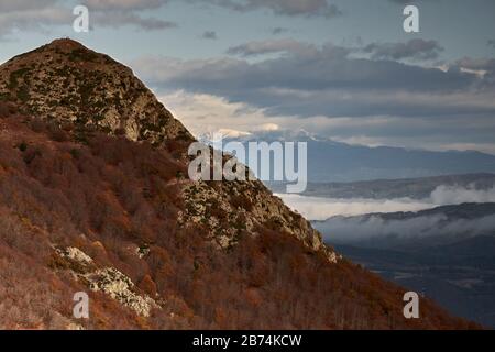 Mountain peak in autumnal forest, snowy mountains in the distance and cloudy sky, Montseny, Catalonia, Spain