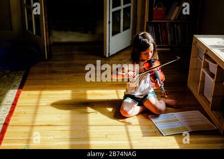 A small child sits alone in a patch of sunlit playing violin