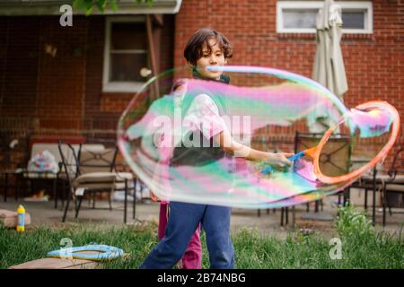 A boy and his sister play with gigantic soap bubbles in the back yard Stock Photo