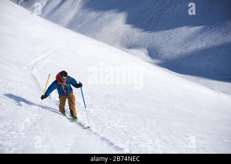 Man in blue jacket ski touring uphill Stock Photo