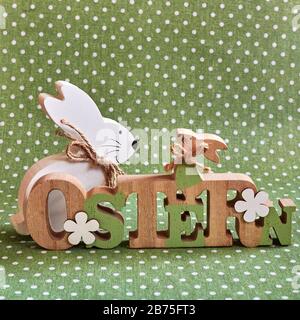 Wooden Easter bunny in front of a green background with white dots. The Text is German for Easter. Stock Photo