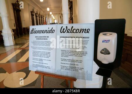 Texas, USA. 13th March, 2020. Bilingual signs warning of coronavirus greet visitors at the Texas Capitol in Austin, where Gov. Greg Abbott held a press conference earlier declaring a statewide 'state of disaster' while Texas braces for an onslaught of coronavirus cases. A hand sanitizer dispenser sits next to the signs Credit: Bob Daemmrich/Alamy Live News Stock Photo