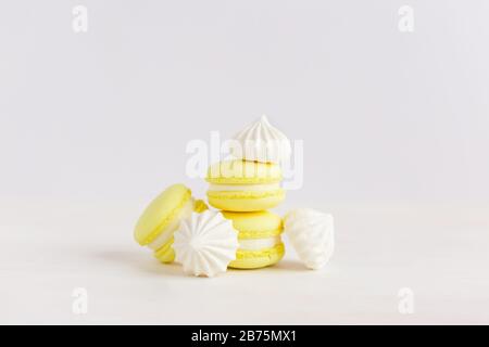 Yellow french macarons and white marshmallows on a white wooden background. Place for text. Stock Photo