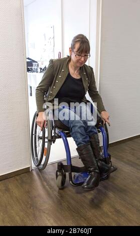 Young disabled woman in a wheelchair opens an entrance door on 18.01.2017. Often doors in public buildings are not suitable for disabled people, because they do not have a width for wheelchairs. [automated translation] Stock Photo