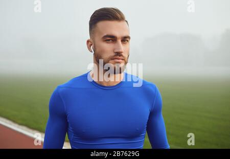 A sports guy in blue clothes smiles while looking at the stadium in the fog Stock Photo