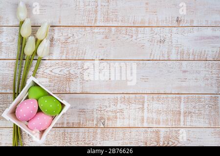 Easter background with colorful eggs and tulips over white wooden table - copy space Stock Photo