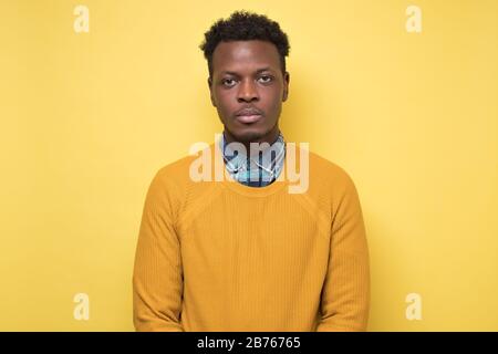 Young african american man in yellow sweater looking serious at camera. Stock Photo