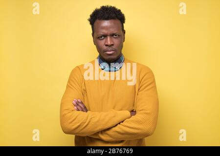Young african american man in yellow sweater looking serious at camera. Stock Photo