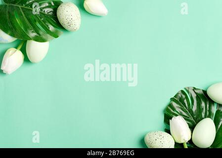Easter festive card from fresh green tropical leaf of Monstera plant, green eggs and small quail eggs on a light turquoise background, copy cpace. Hap Stock Photo