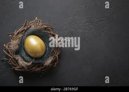 Chicken golden egg in nest on black. Easter dark background. Top view and copy space. Stock Photo