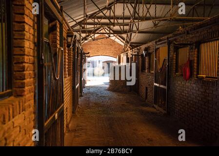 Inside a bricks stable looking trough a door  two hay rolls and horses stals Stock Photo