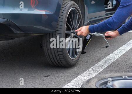 Close up mans hands changing a wheel using screwdriver. Replacing winter and summer tires. Seasonal tire replacement concept. Service process. Prague Stock Photo