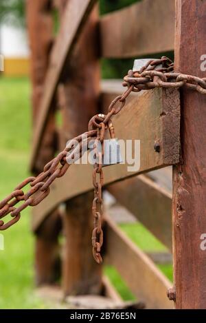 Padlock with a chain rusted on a wooden fence with grass background with selective focus on the padlock Stock Photo