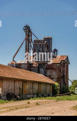 Big, rusted and old iron machinery with barns or storage places next to a train station Stock Photo