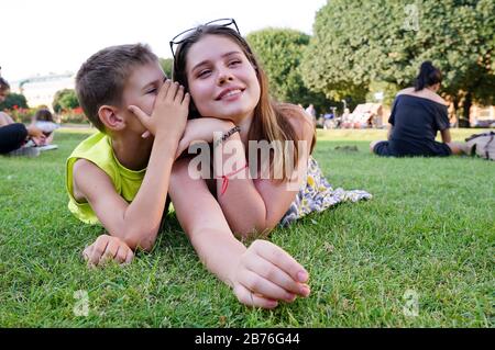 A young guy whispers in the ear of a girl on a green lawn Stock Photo