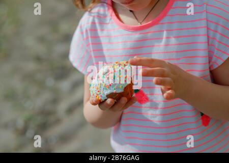 small cupcake similar to an Easter panettone in hands of girl in pink T-shirt. Easter pasha and kulich. Spring sunny day. happy family preparing for E Stock Photo