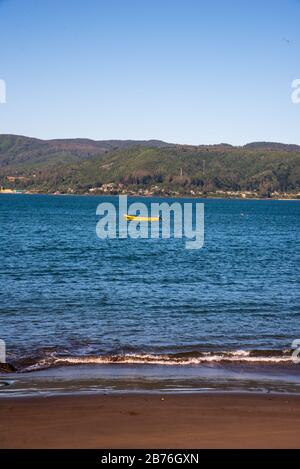 Shore view of the Pacific Ocean, a yellow fisher boat and a mountain range Stock Photo