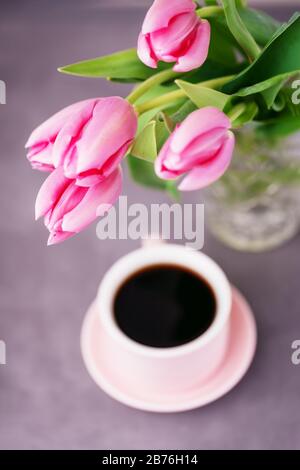 Black coffee in a pink cup and pink spring tulips on a gray background. Top view Stock Photo