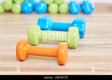 three small rubberized dumbbells of different weights lie on the floor against the background of sets of the same dumbbells in the background Stock Photo