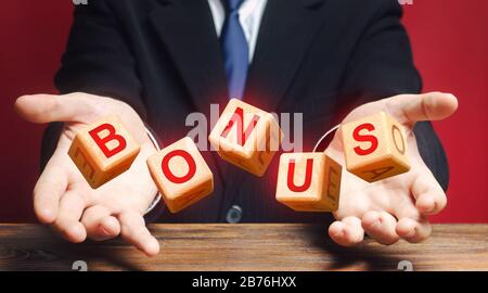 Cubes thrown by a man make word BONUS. Receive bonuses, rewards and preferences. A nice addition. Salary increase, wage premium for holidays. Favorabl Stock Photo