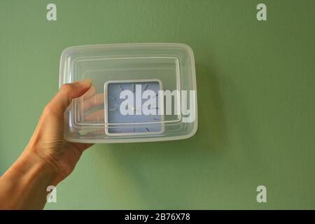 Hand holding a closed plastic box with analog clock inside it. Timesaving, have a good time concept metaphor