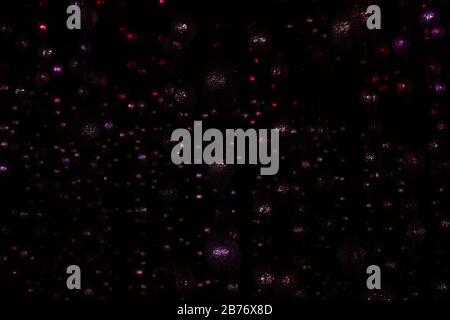 Abstract Festive Christmas dark purple pink red garland lights on black background. Defocused Glowing light bulb garland, copy space. Elegant backdrop Stock Photo