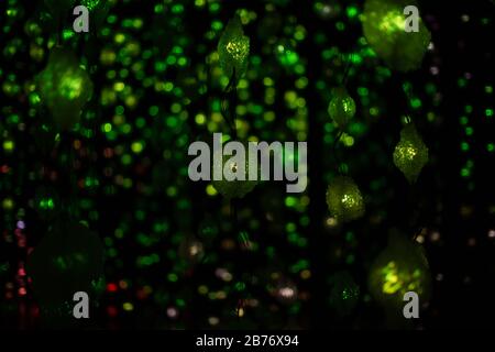 Abstract Christmas green garland lights on black background. Defocused Glowing light bulb garland, copy space. Stock Photo