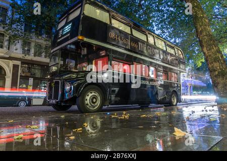A black Routemaster double decker bus of The Ghost Tours company parked on a London street on a rainy evening
