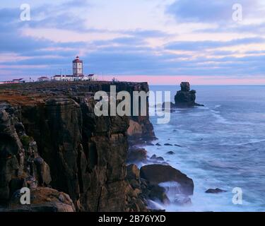 Lighthouse over the cliff on cloudy sunset Stock Photo