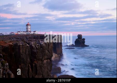 Lighthouse over the cliff on cloudy sunset Stock Photo