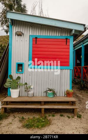 Tin storage house with a red wooden window and light blue moldings and some cactus on front Stock Photo