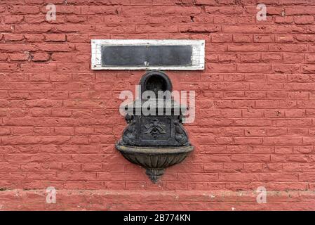 Antique drinking fountain - sprue - spout on a train station with a blank sign and a red wall made of bricks Stock Photo